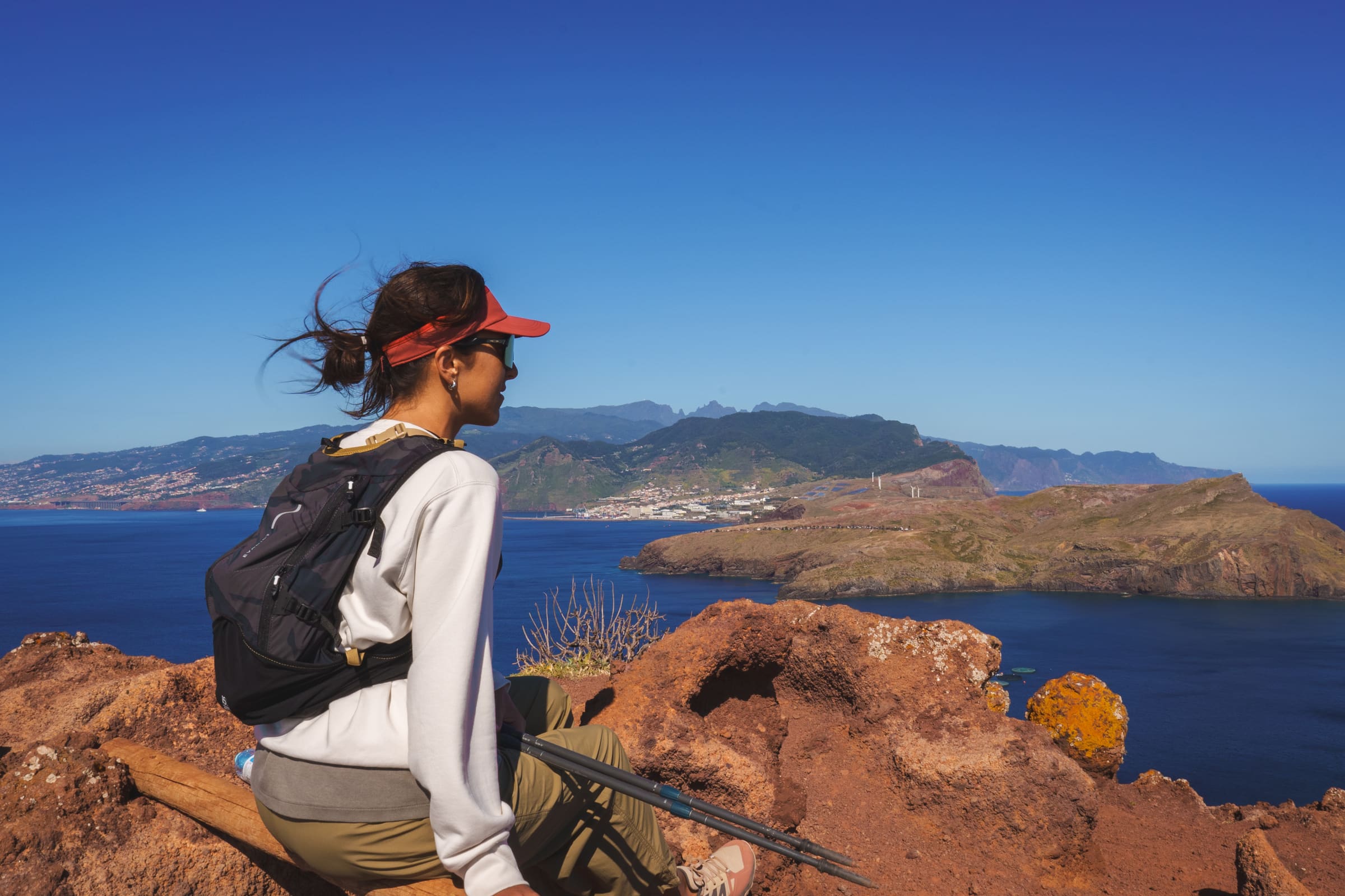 A hiker resting on the volcanic cliffs of Ponta de São Lourenço, Madeira, looking out over the peninsula, the Atlantic, and the mountains beyond.